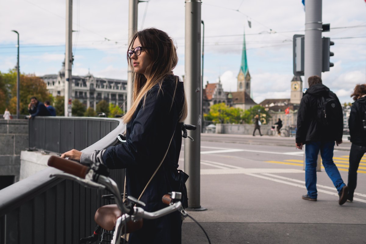 Woman with her bicycle waiting at a tram-lined street crossing in Zurich