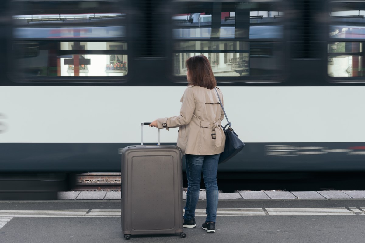 Woman with a suitcase waiting on a platform as a train passes in Geneva