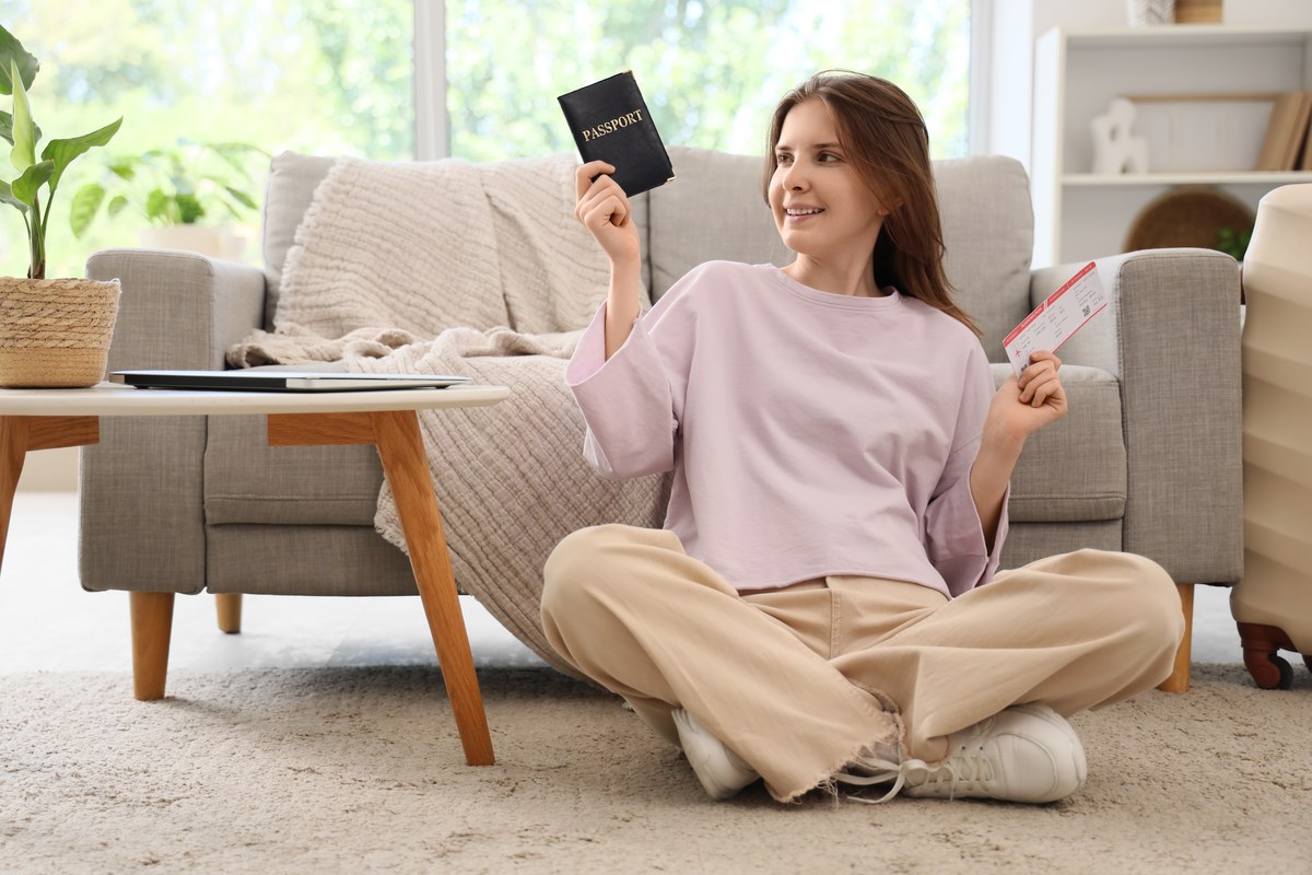 Smiling woman sitting on the floor at home holding a passport and a ticket