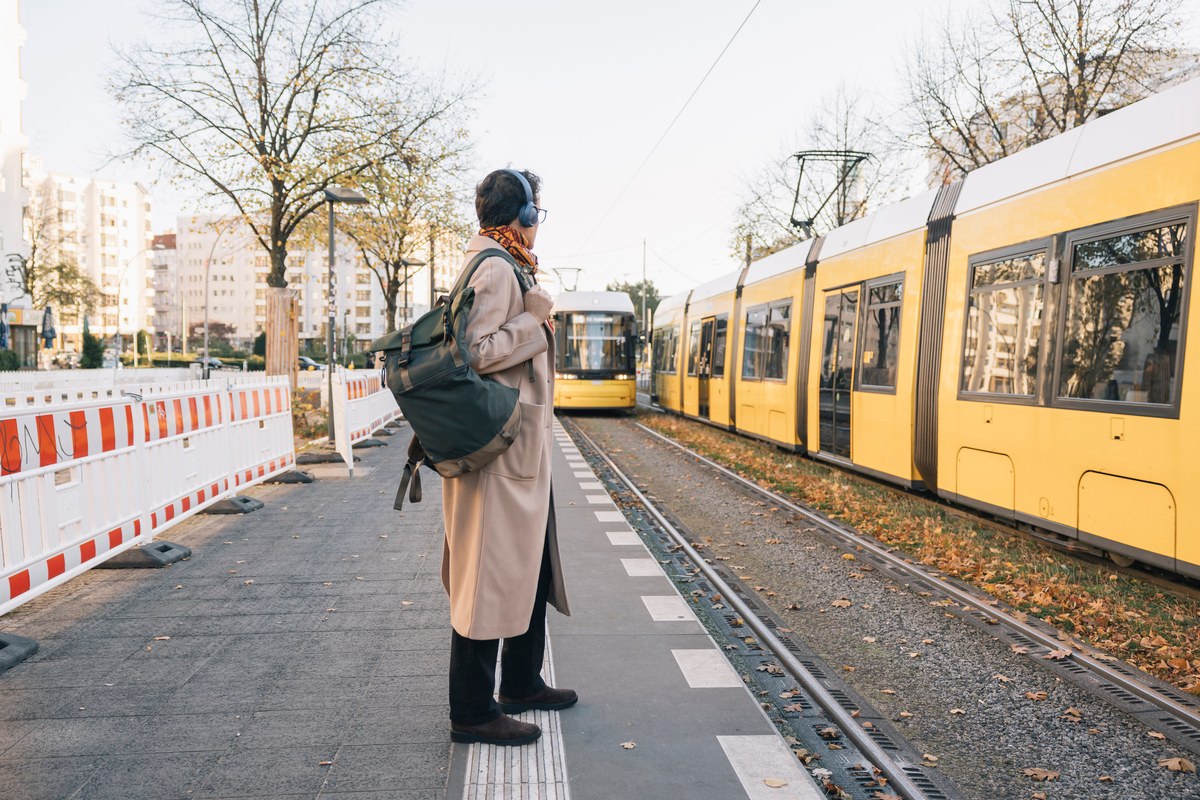 Woman with backpack and headphones waiting at a Berlin tram stop as yellow trams arrive