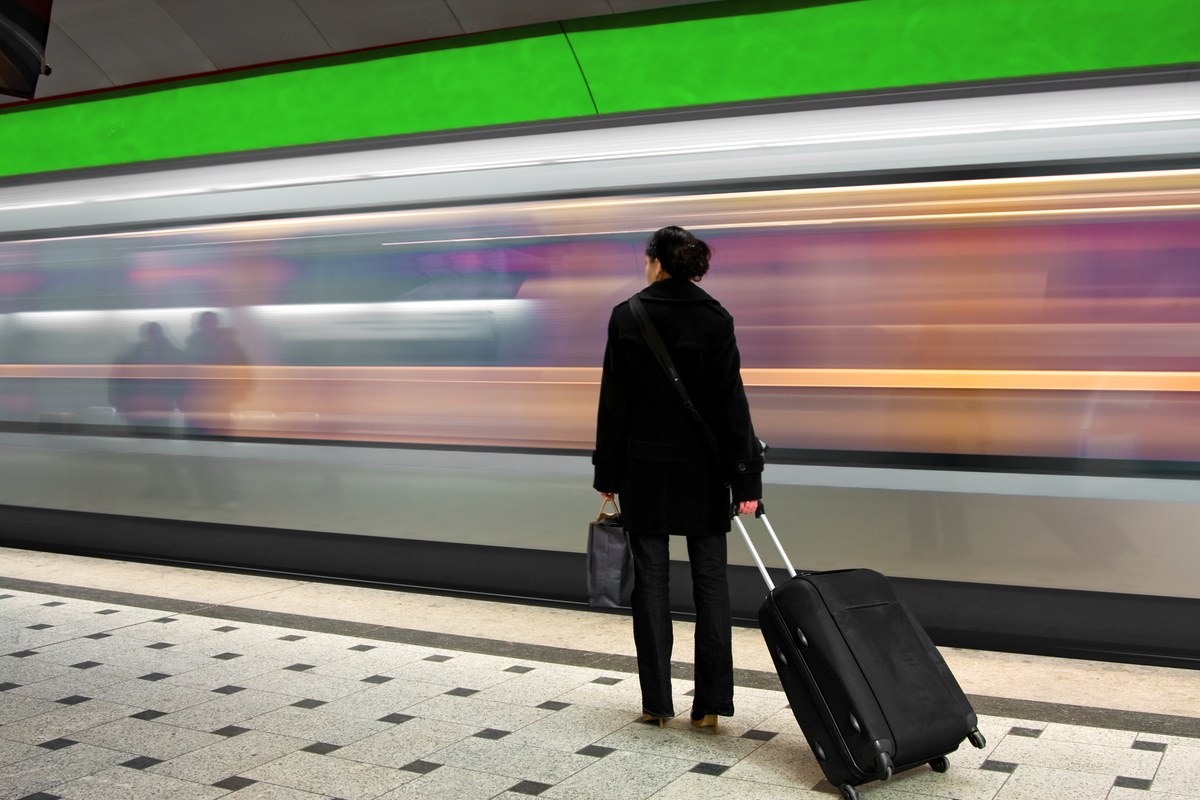 Woman with a suitcase on a subway platform as a train rushes past