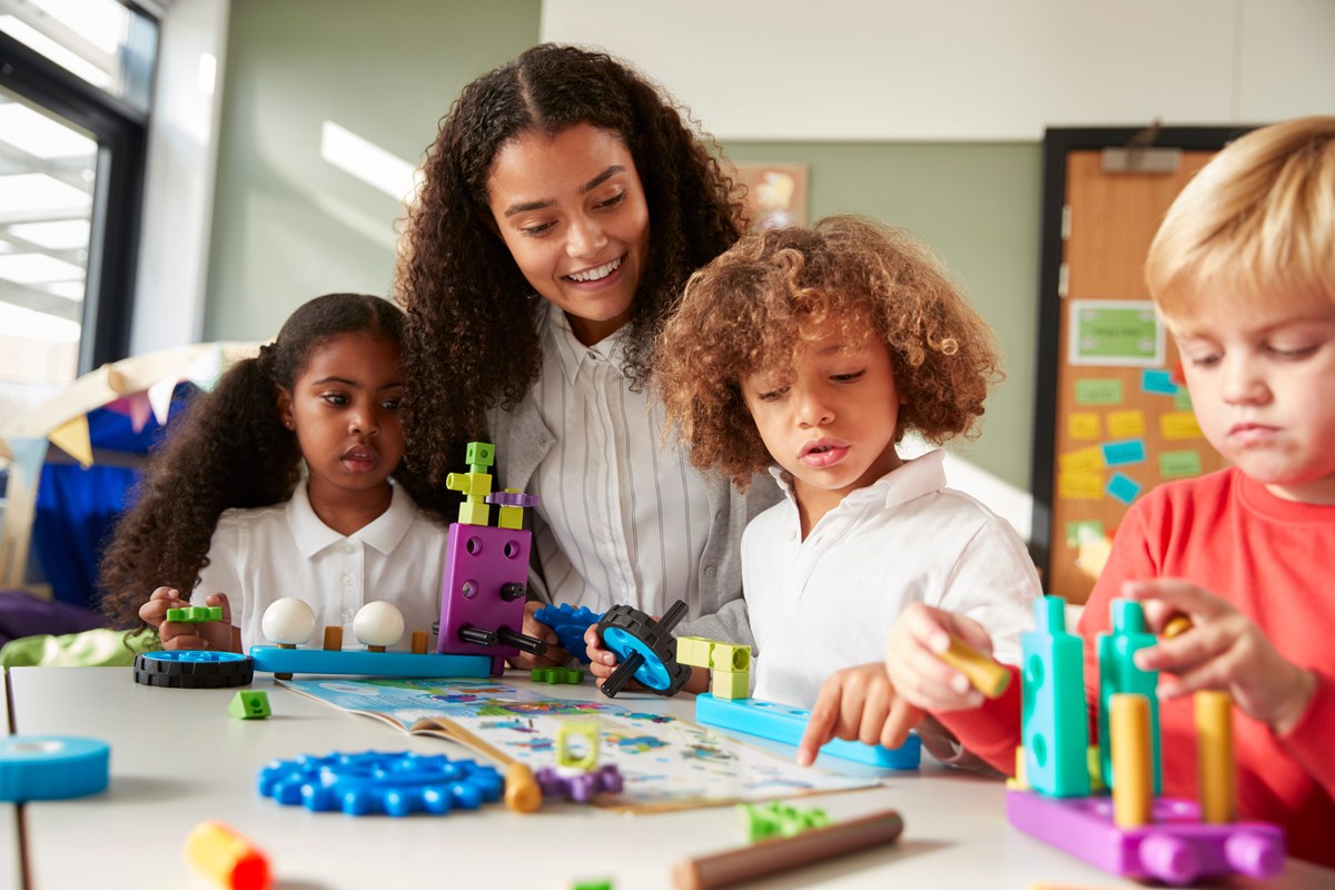 Kindergarten teacher building with construction toys alongside three children