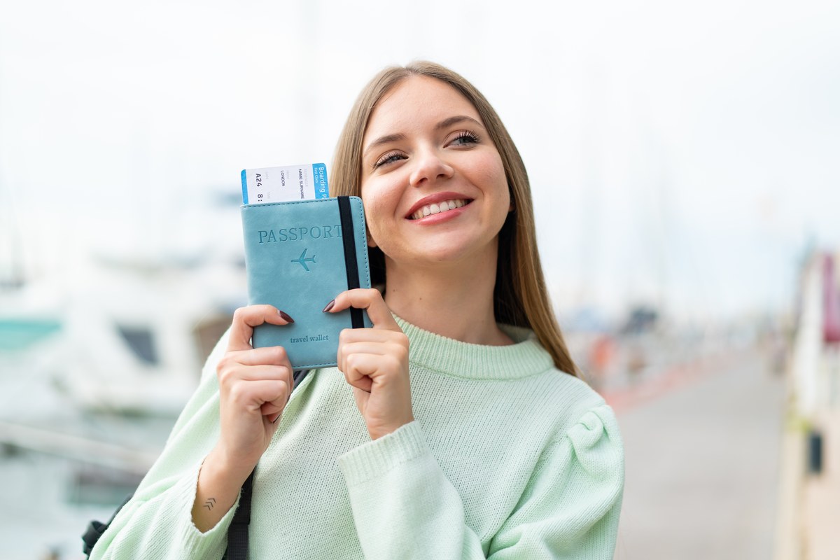 Smiling young woman holding up a passport with a boarding pass