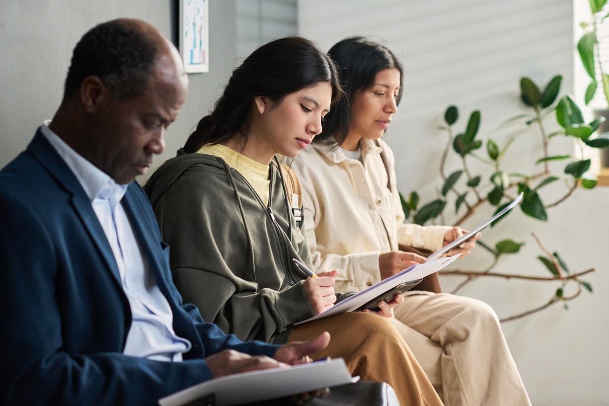 Two young women and a man filling in forms in a visa centre waiting area
