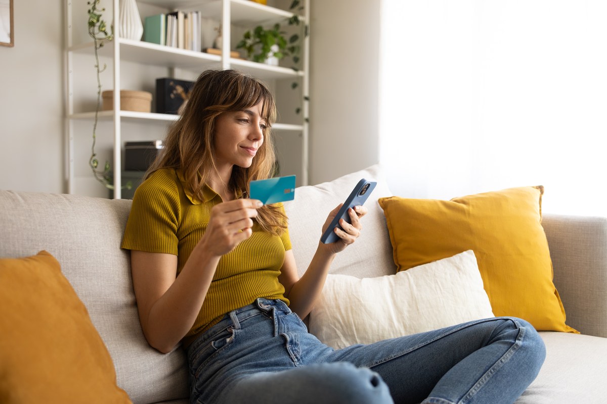 Woman on a sofa holding a bank card and a smartphone