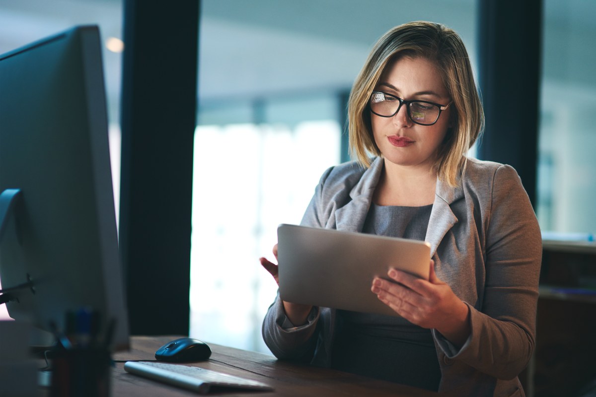 Woman with glasses working on a tablet at an office desk