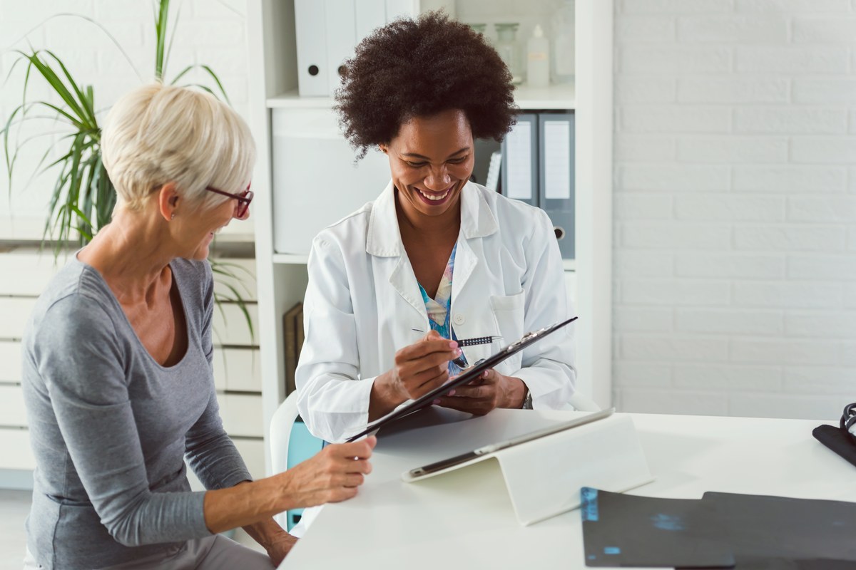 Female doctor taking notes while talking with an older female patient