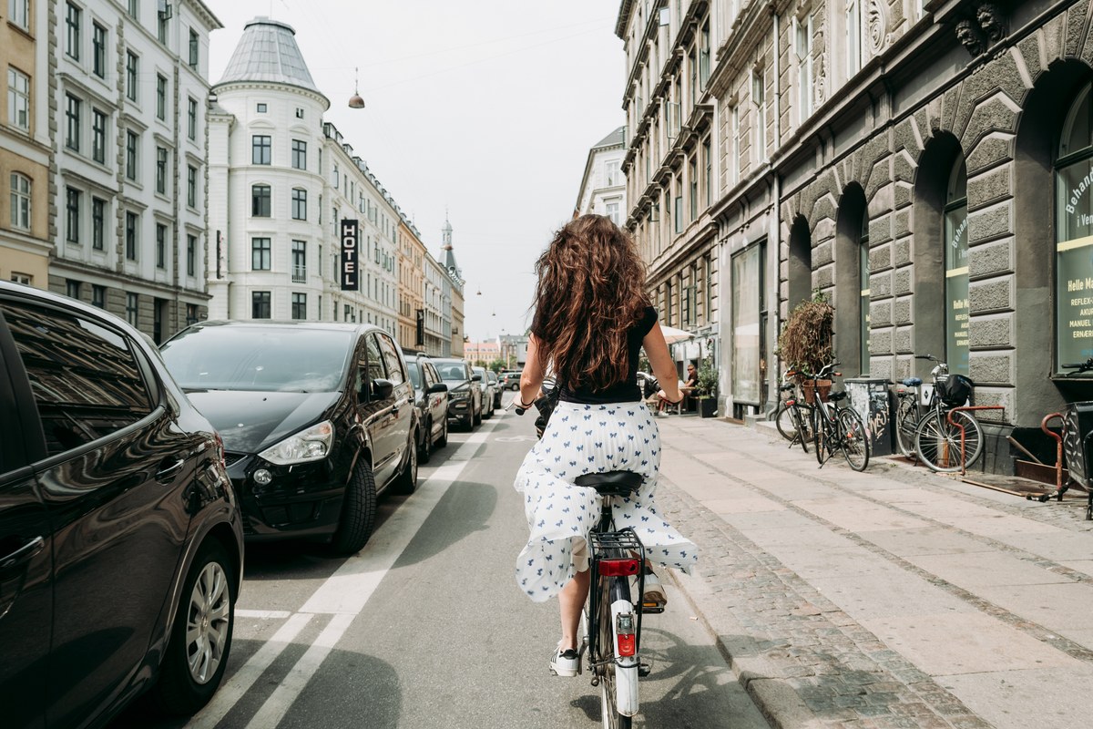 Woman cycling in a bike lane between parked cars and apartment buildings in Copenhagen
