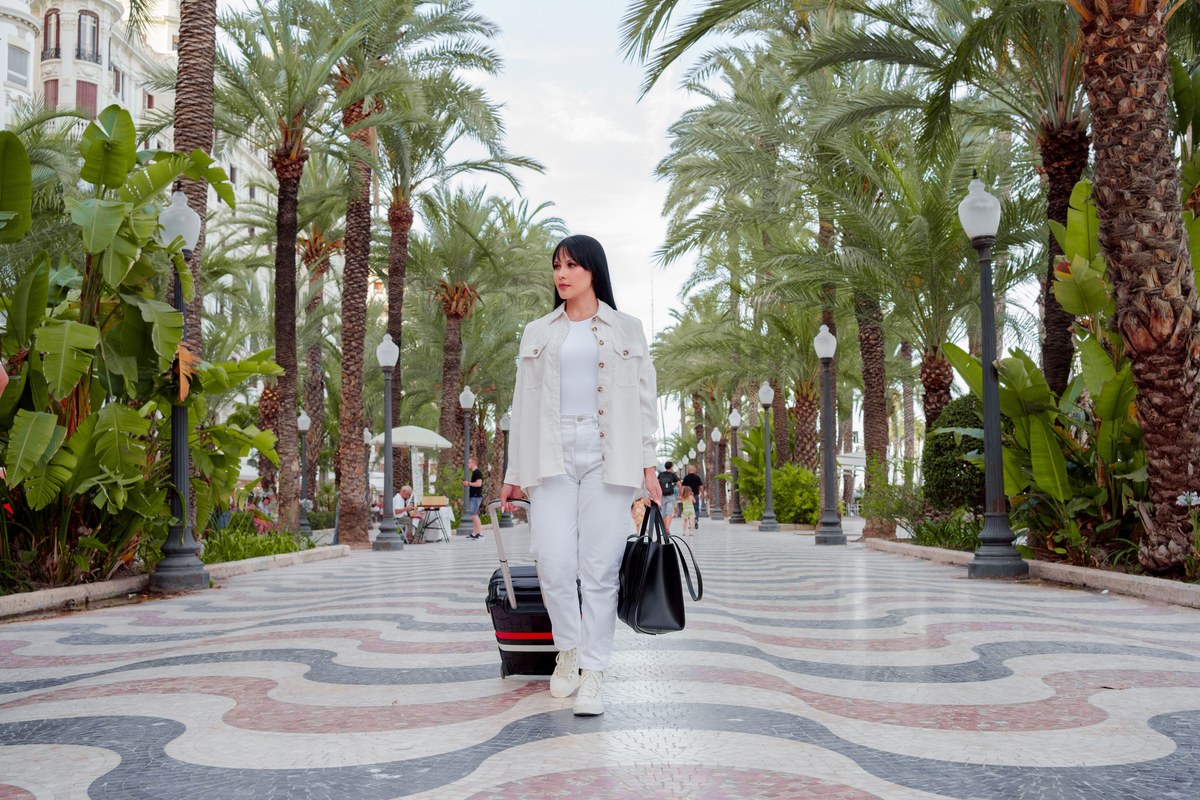 Woman pulling a suitcase along a palm-lined promenade with wavy mosaic paving