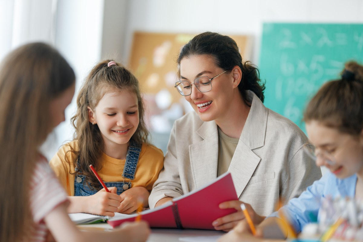 Teacher smiling as she helps a group of girls with their schoolwork