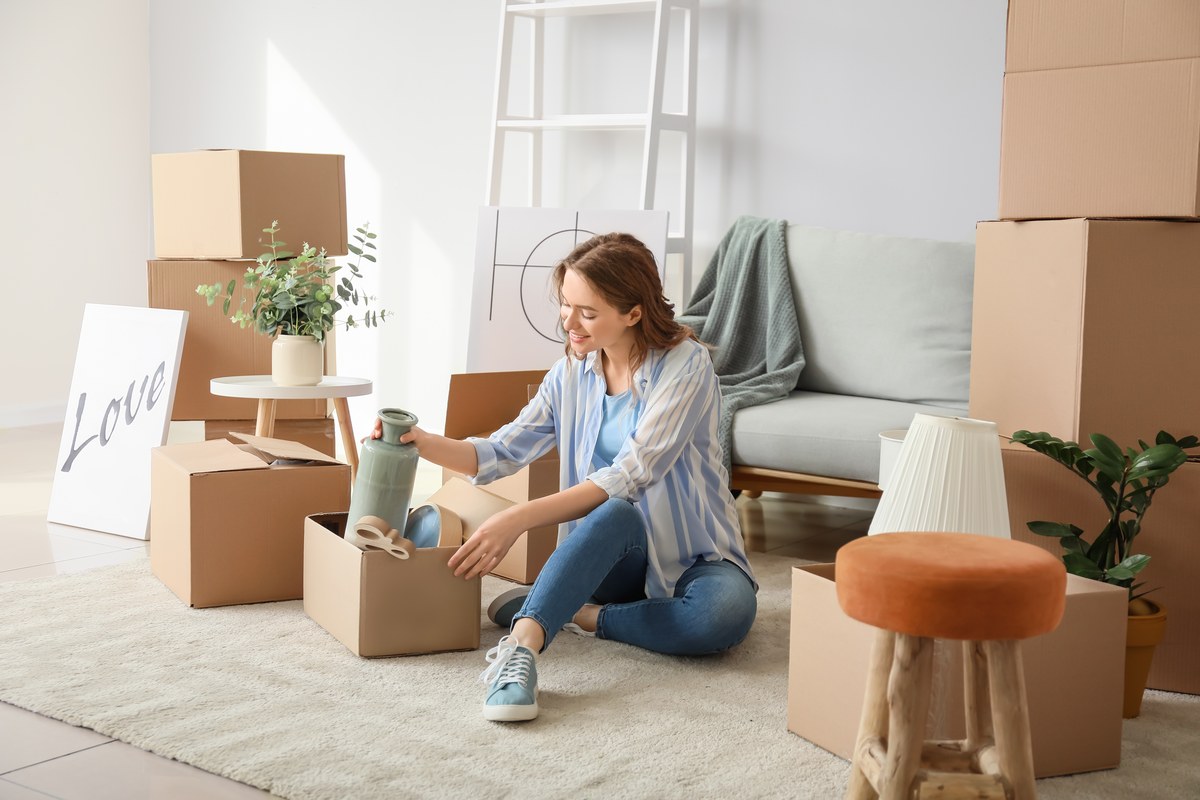 Woman sitting on the floor unpacking moving boxes in a bright living room