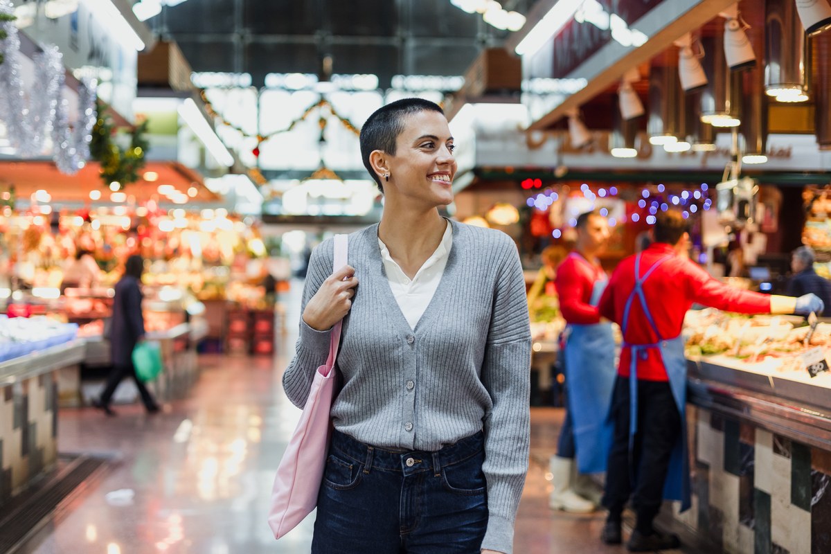 Smiling woman with a shopping bag walking through an indoor food market