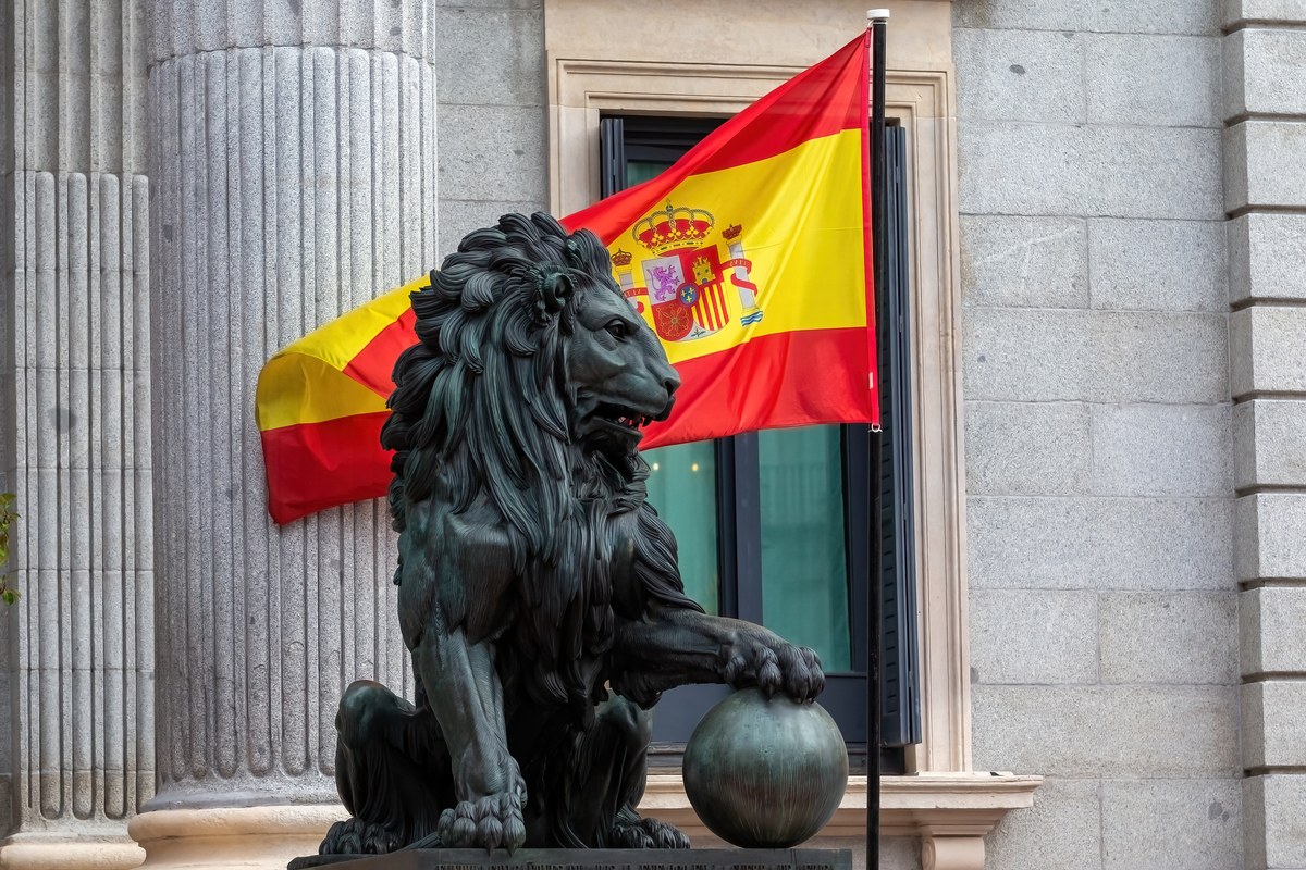 Spanish flag behind a bronze lion statue at the Congress of Deputies in Madrid