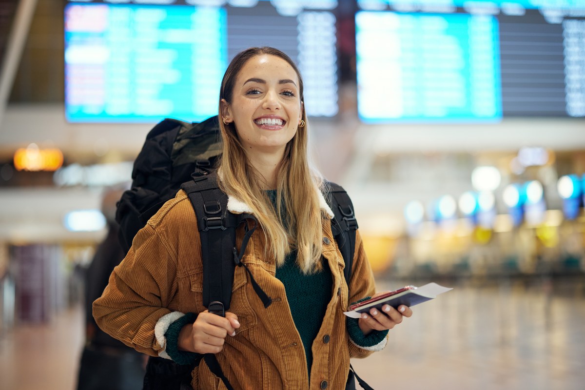 Smiling woman with a backpack holding a passport and ticket at an airport