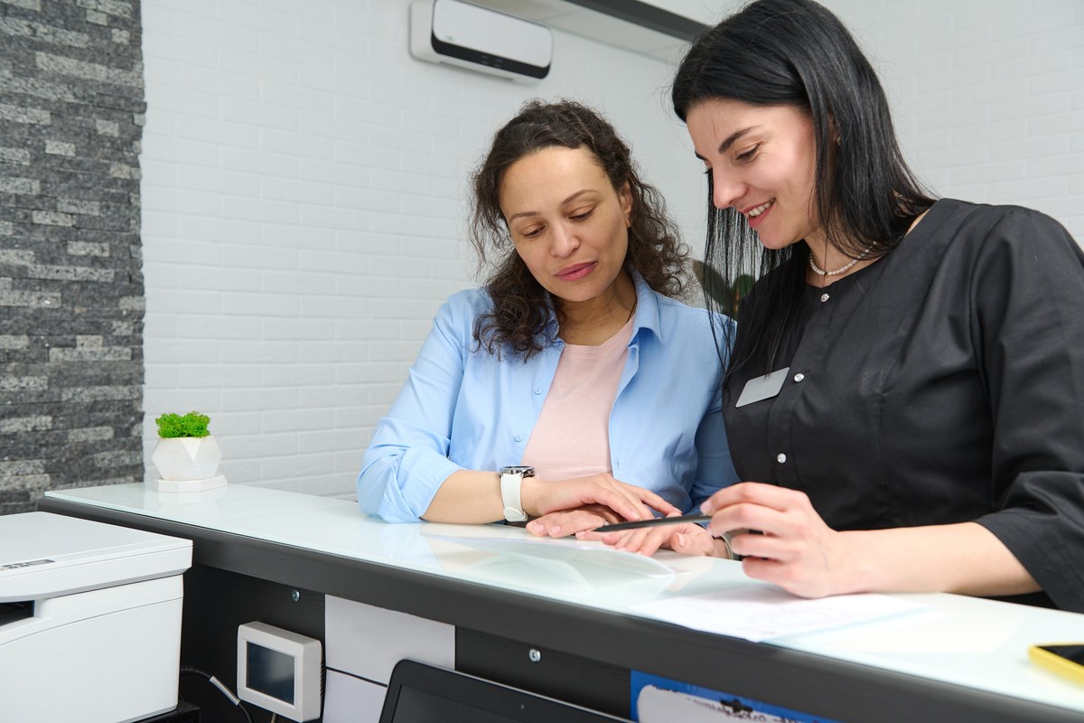 Woman filling in a form at a reception counter with a staff member