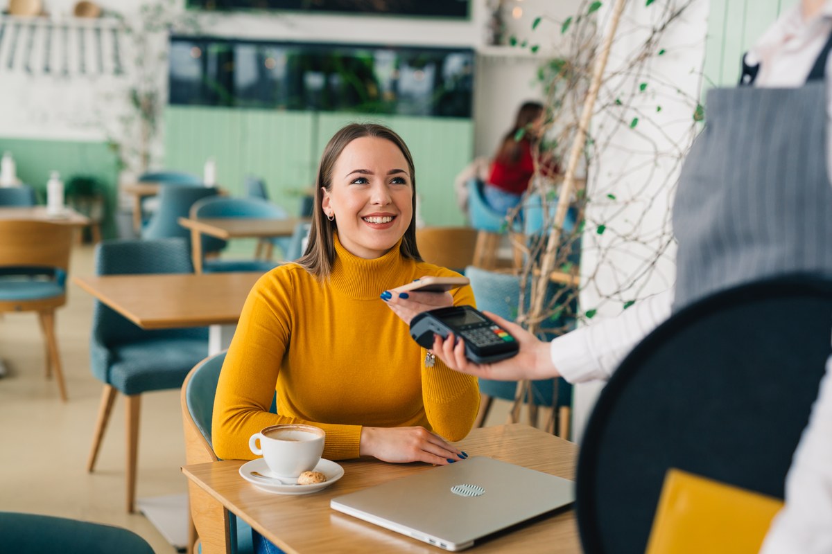 Woman at a café table paying with her phone at a card terminal