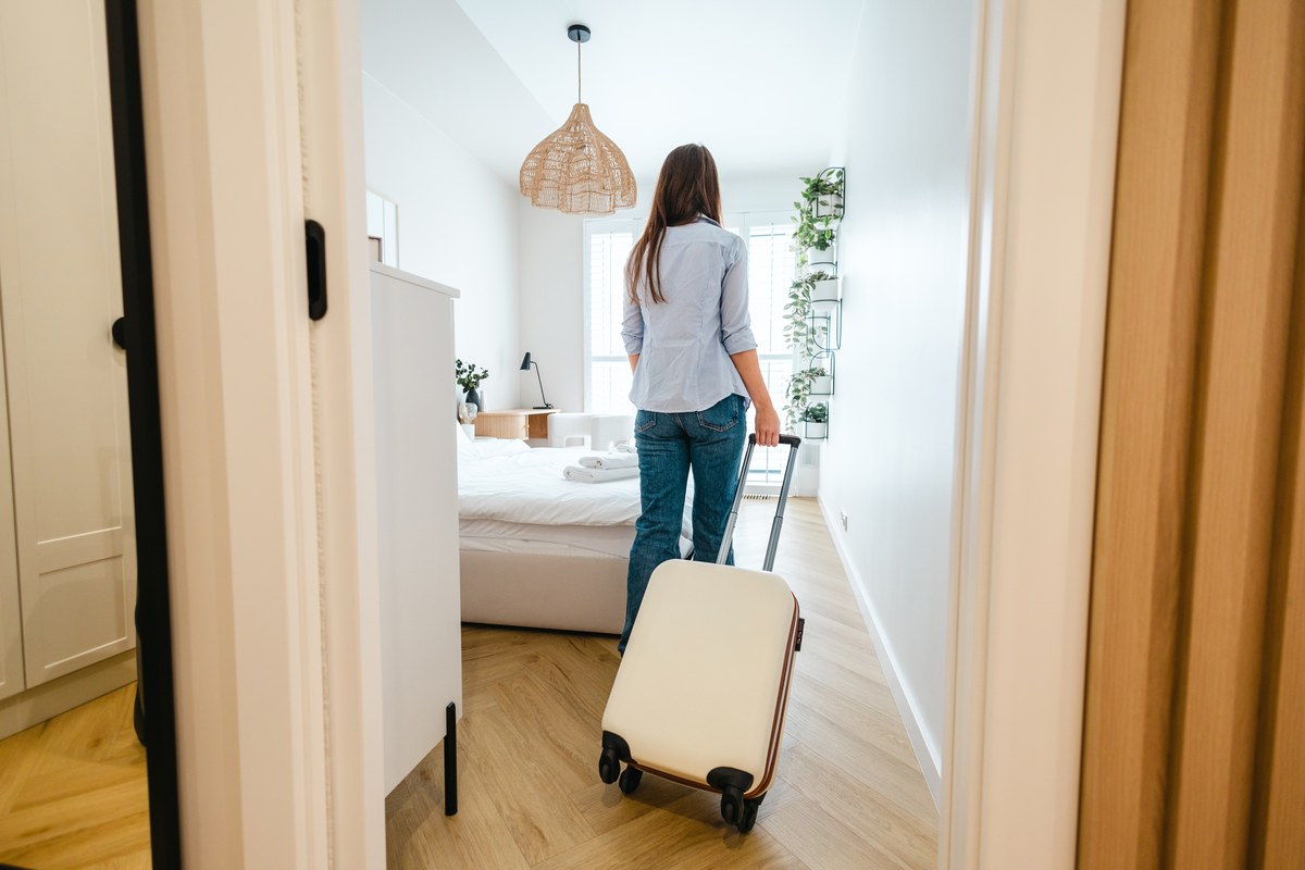 Woman pulling a suitcase into a bright, furnished bedroom