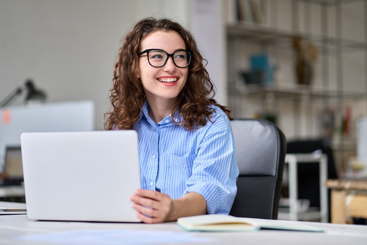 Smiling woman in glasses working on a laptop at an office desk