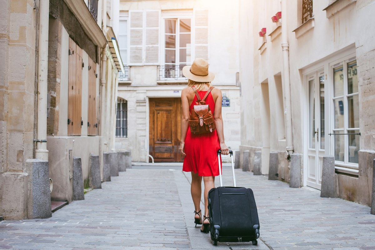 Woman in a red dress pulling a suitcase along a quiet stone-paved street