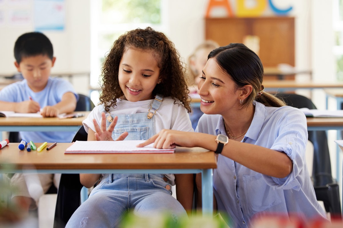 Teacher helping a young girl with her notebook in a classroom