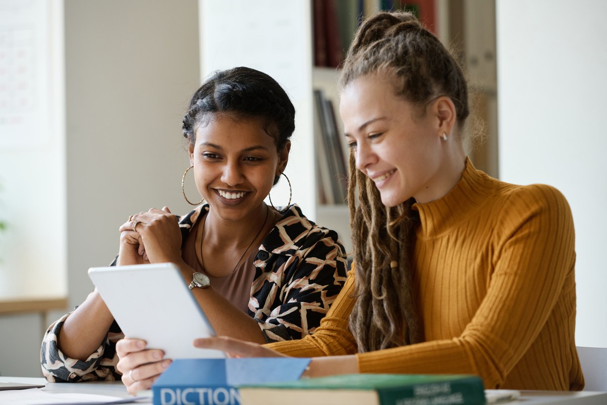 Two young women studying together with a tablet and books