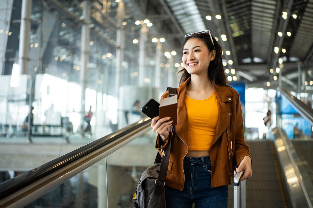 Smiling woman holding a passport and phone at an airport terminal
