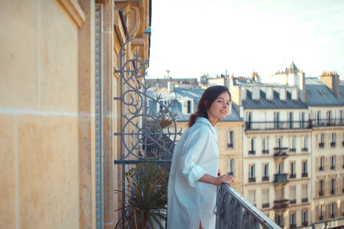 Woman on a wrought-iron balcony overlooking Paris apartment buildings