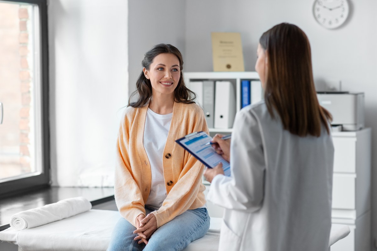 Smiling woman talking to a female doctor holding a clipboard