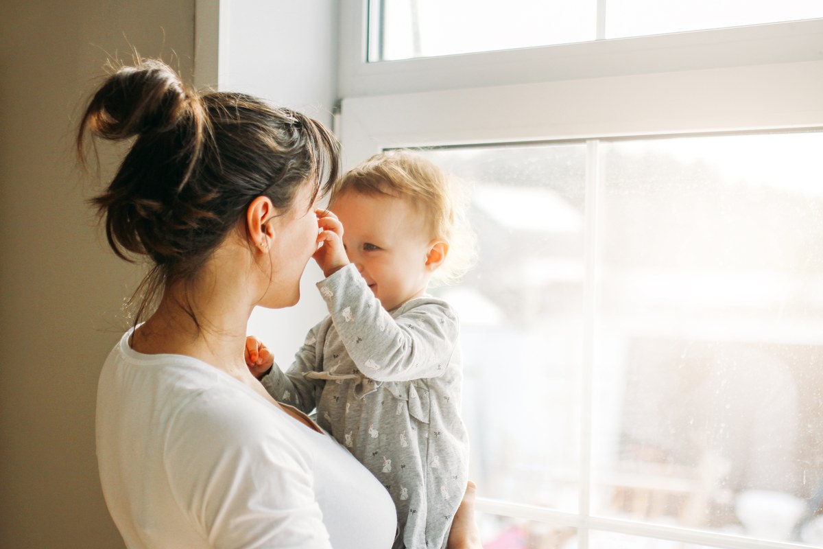Mother holding her baby daughter by a sunlit window