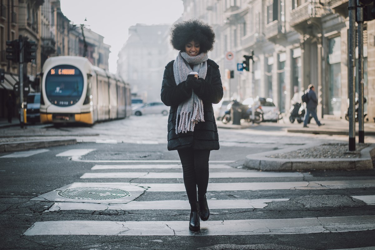 Woman with a coffee crossing a street in Milan as a tram waits behind