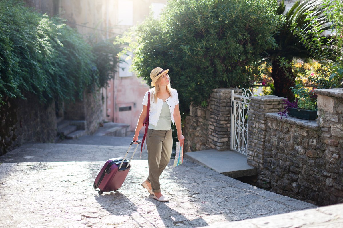 Woman with a suitcase walking along a sunny, narrow Italian street