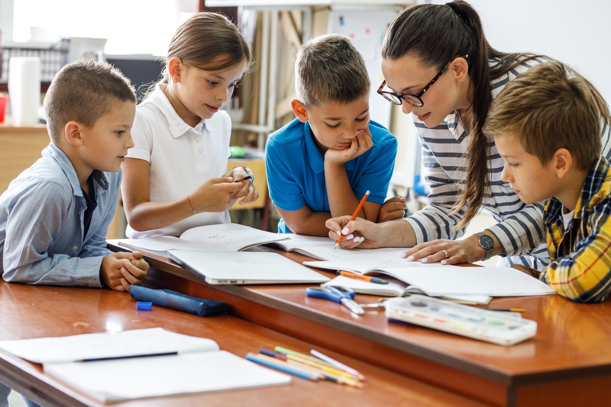 Teacher helping primary school pupils with their work at a classroom table