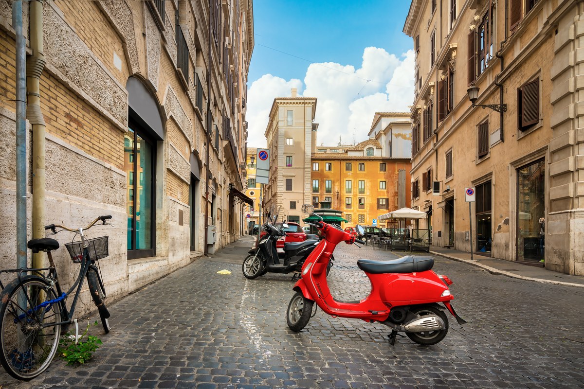 Red scooter parked on a cobbled side street in Rome