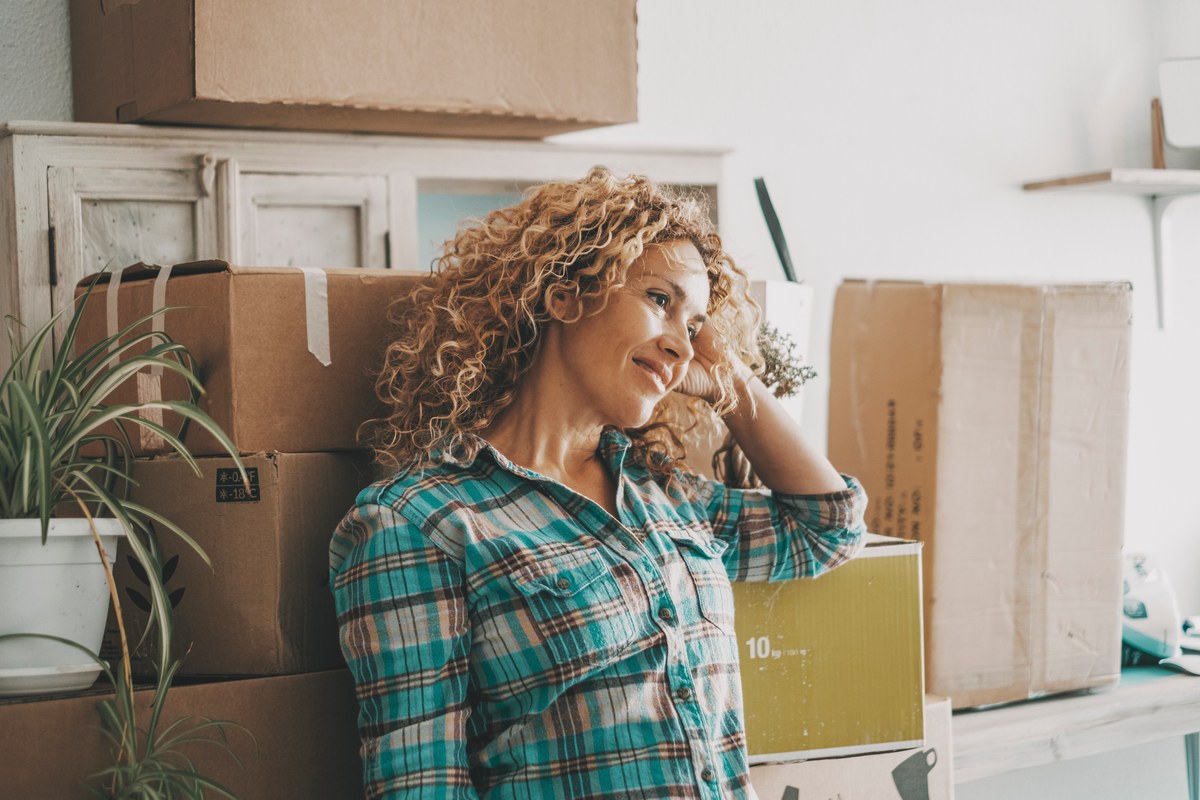 Smiling curly-haired woman leaning against moving boxes in a new home