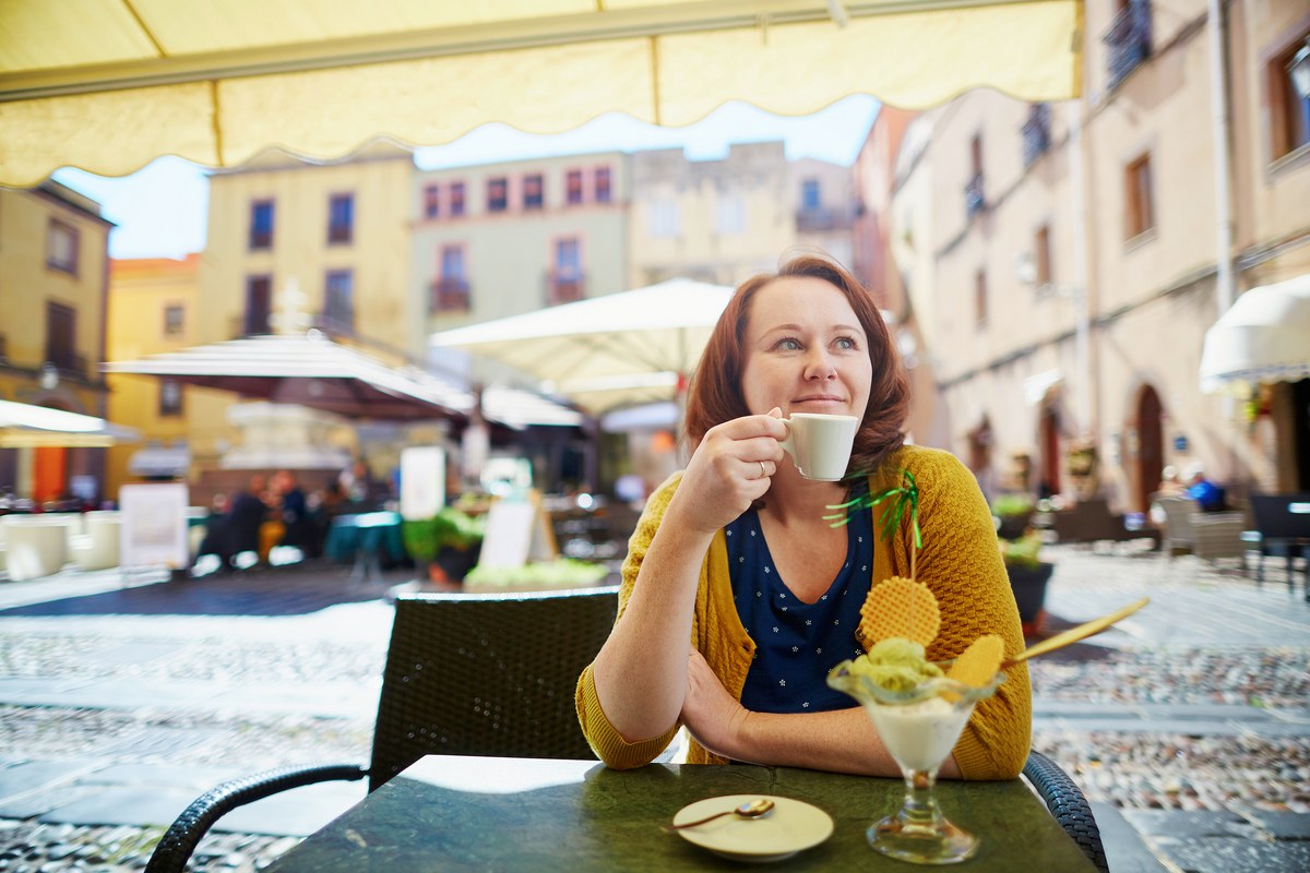 Woman drinking coffee at an outdoor Italian café with an ice cream sundae