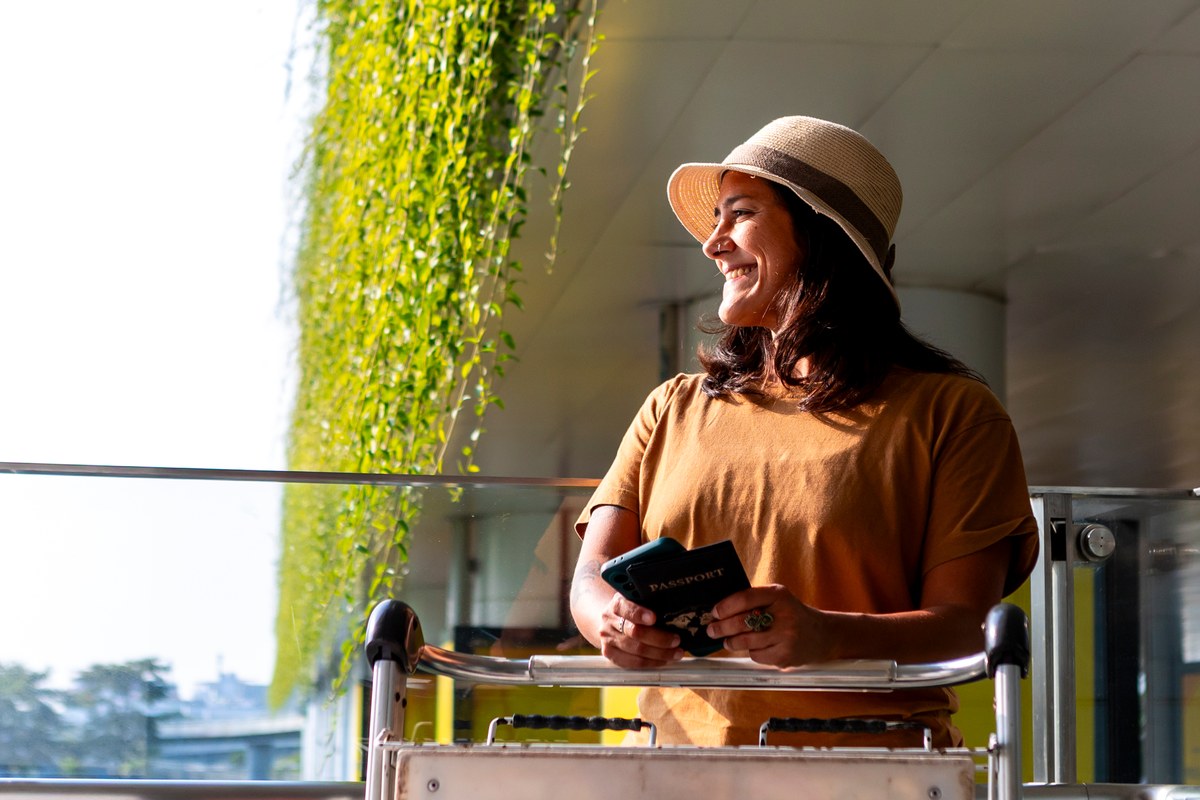 Smiling woman in a straw hat holding a passport at an airport