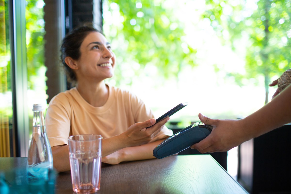 Woman at a café table paying with her phone on a card terminal