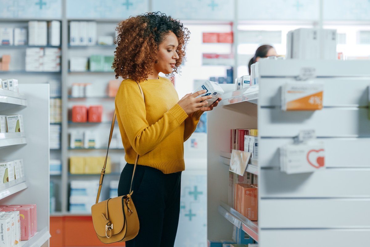 Woman in a yellow sweater reading a medicine box in a pharmacy
