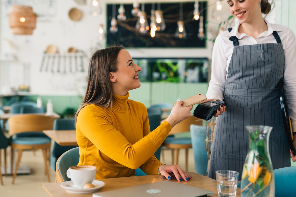 Woman in a yellow jumper paying with her phone at a café counter