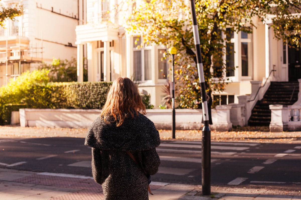 Woman waiting at a zebra crossing opposite white stucco houses on a London residential street