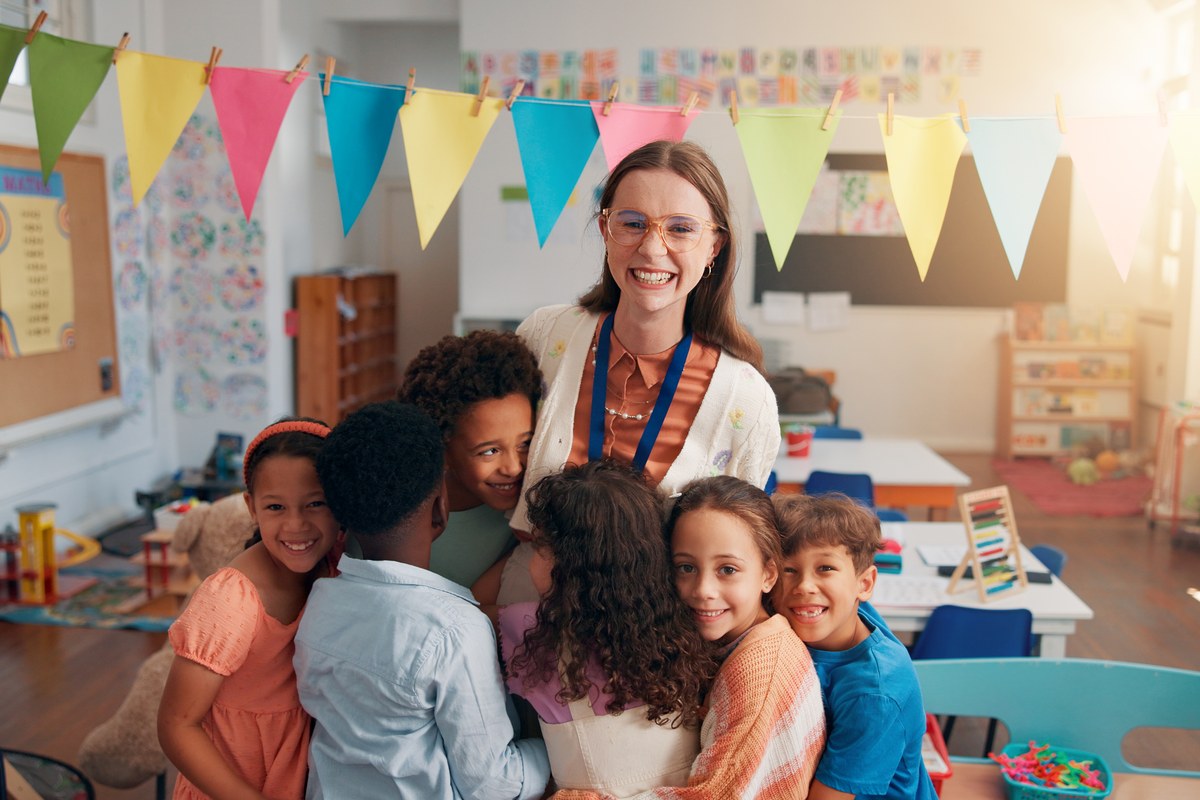 Smiling teacher hugged by a group of children in a colourful classroom