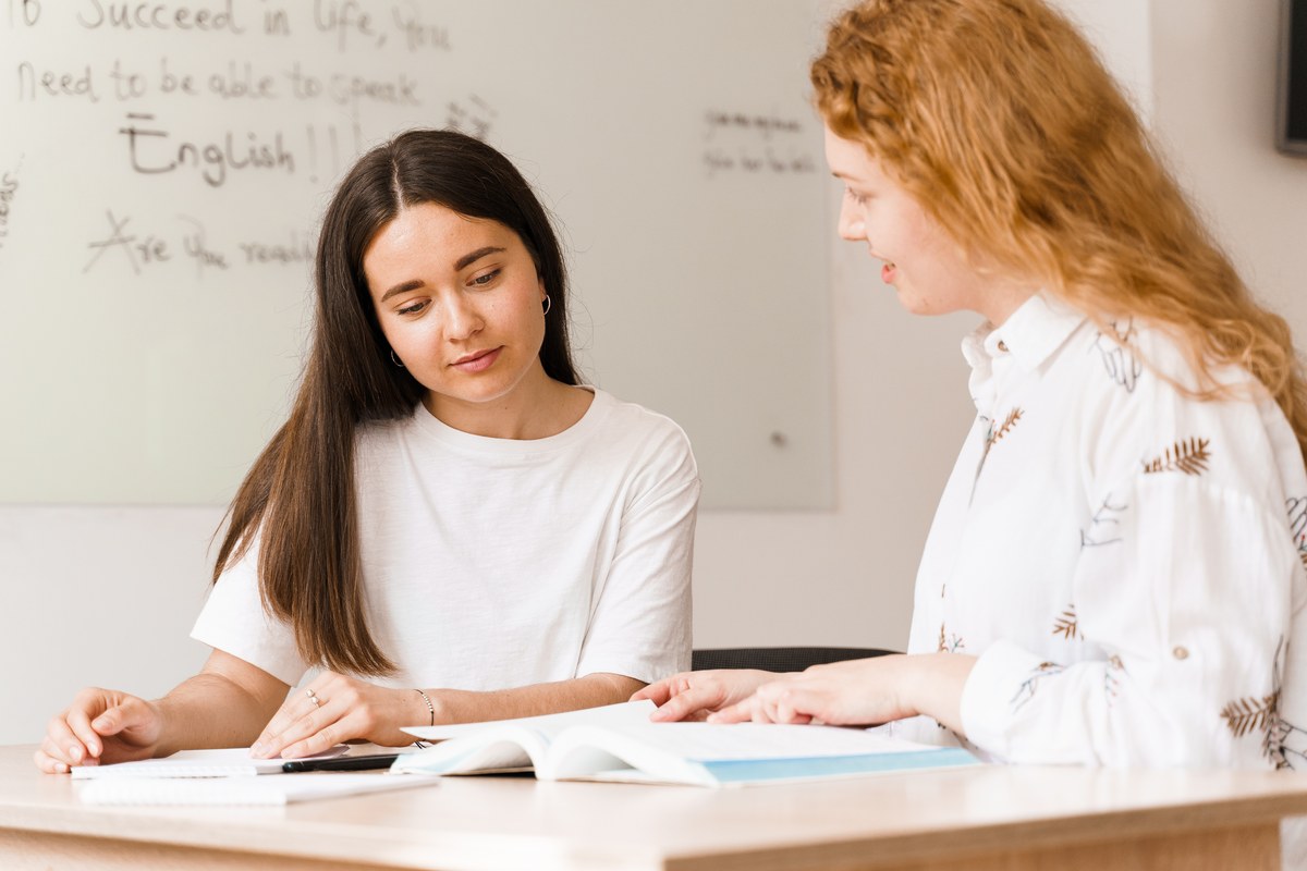 Young woman studying with a book beside a teacher in an English class