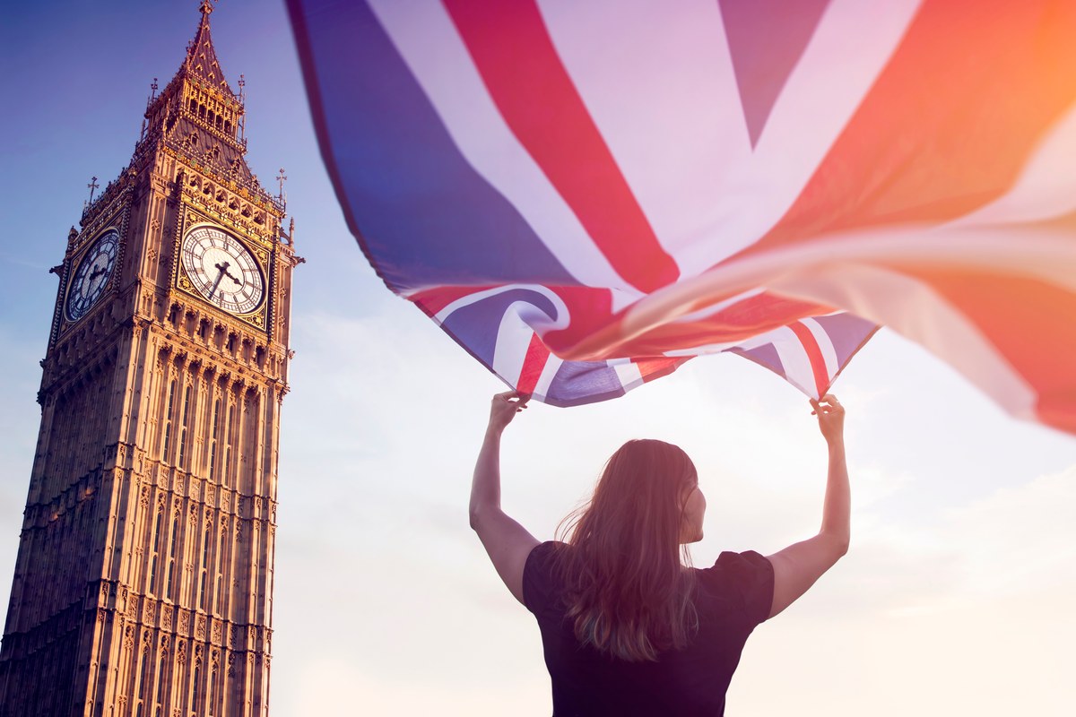 Woman holding up a Union Jack flag beside Big Ben in London