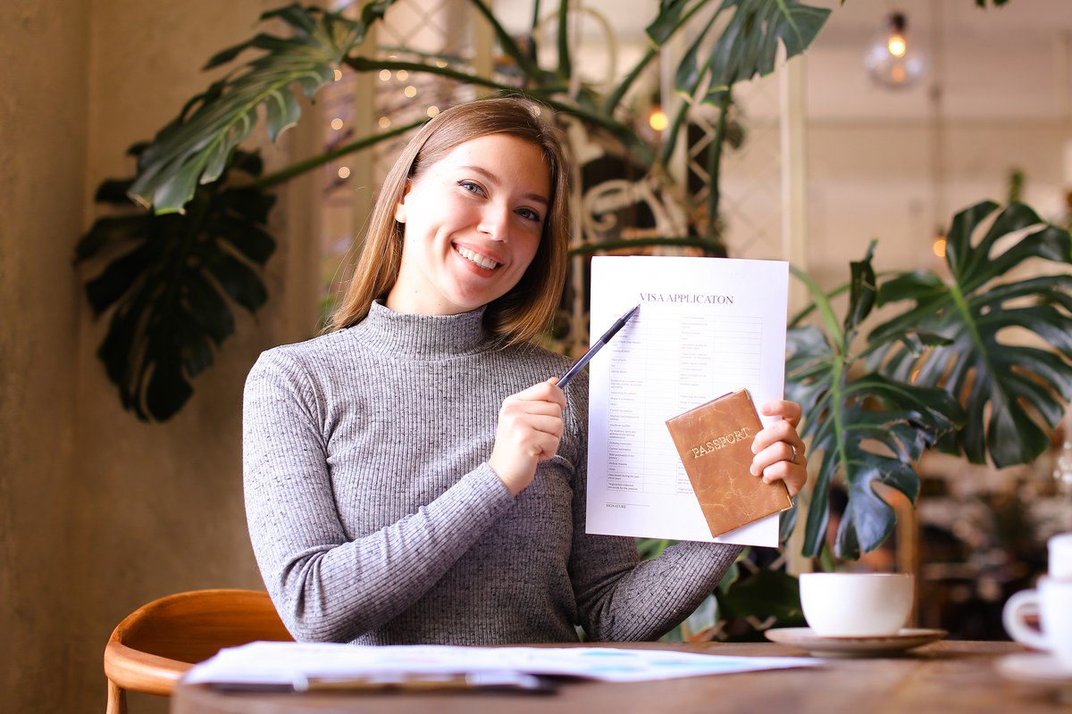 Smiling woman holding a passport and a visa application form at a café table