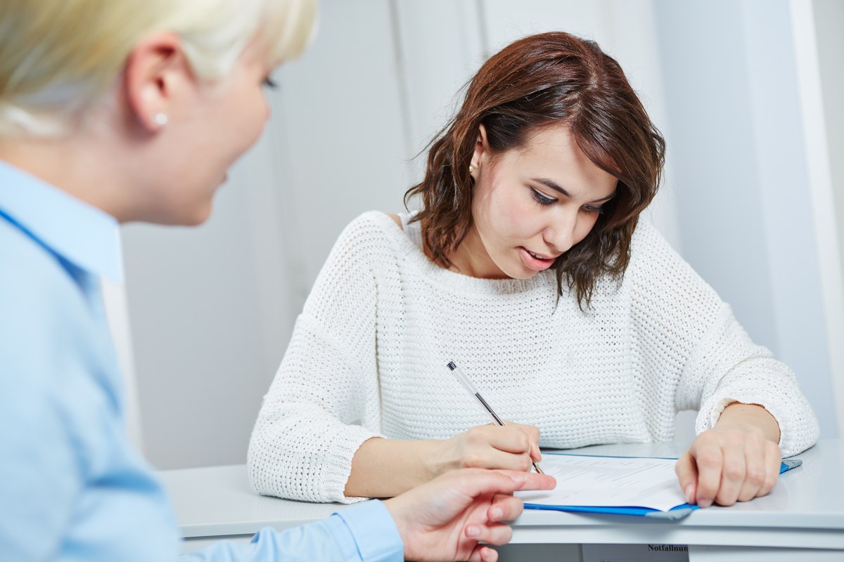 Woman filling in a form at a counter while a staff member looks on
