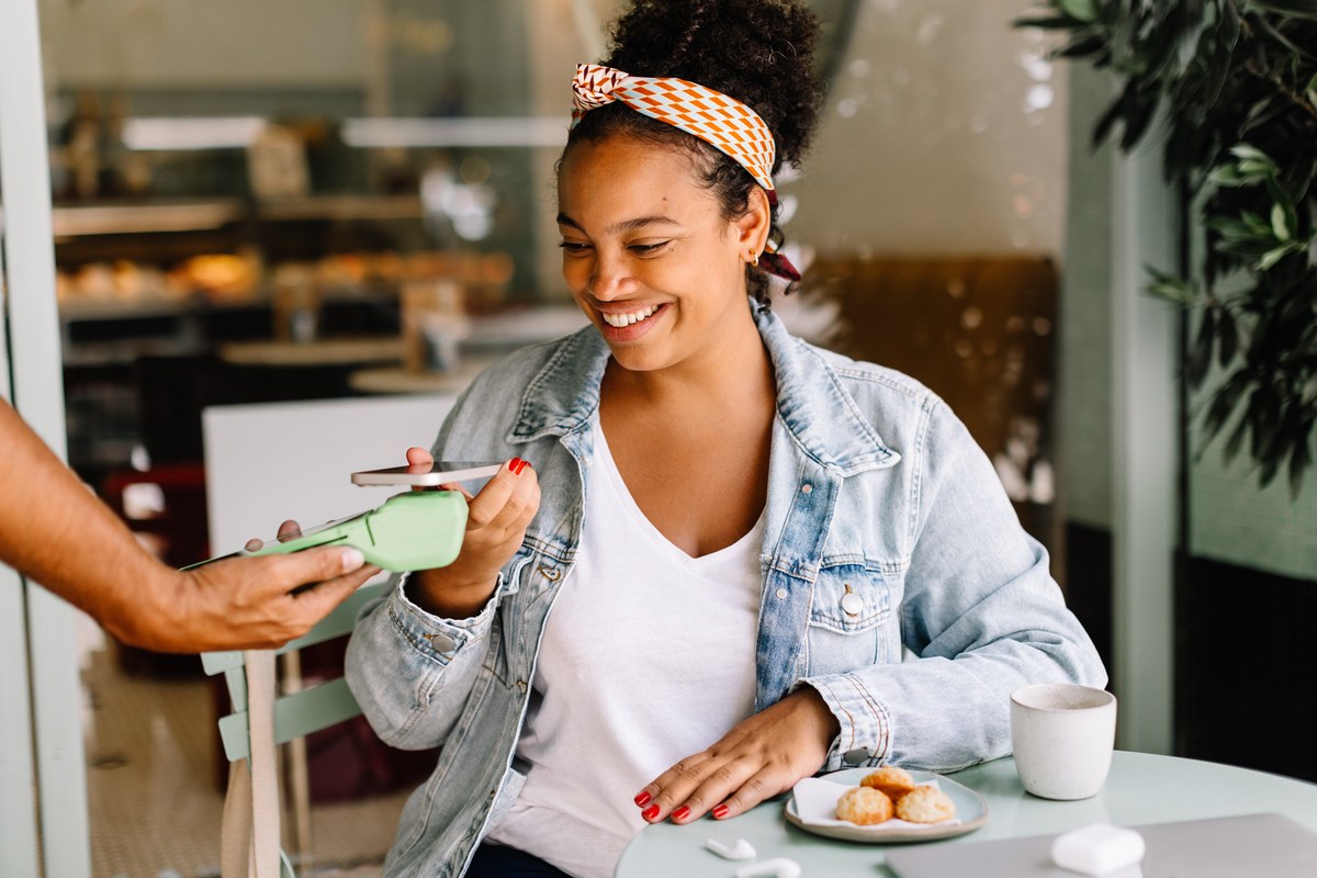 Smiling woman paying with her phone on a card terminal at a café table