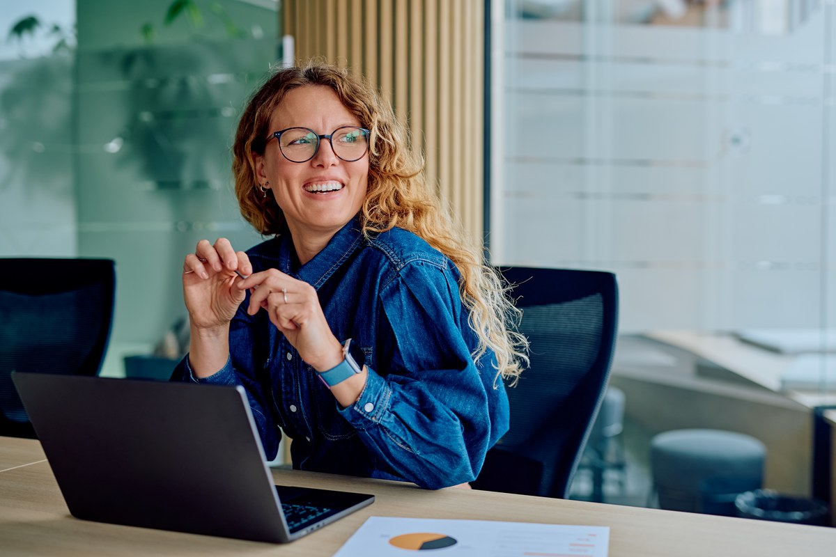 Smiling woman with glasses at a laptop in an office