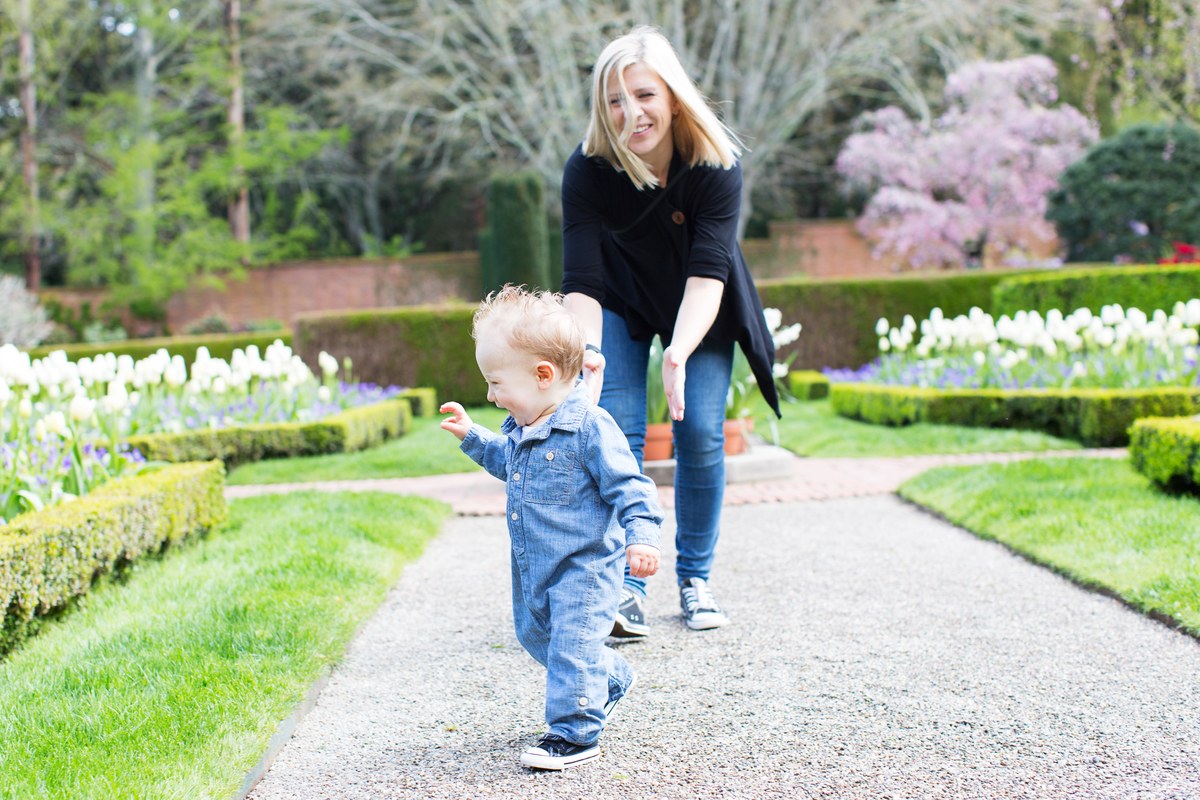 Mother walking behind her toddler on a garden path in spring