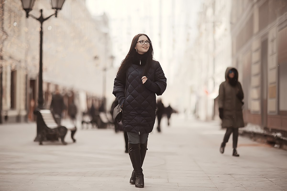 Woman in a black winter coat walking along a city street lined with pale buildings