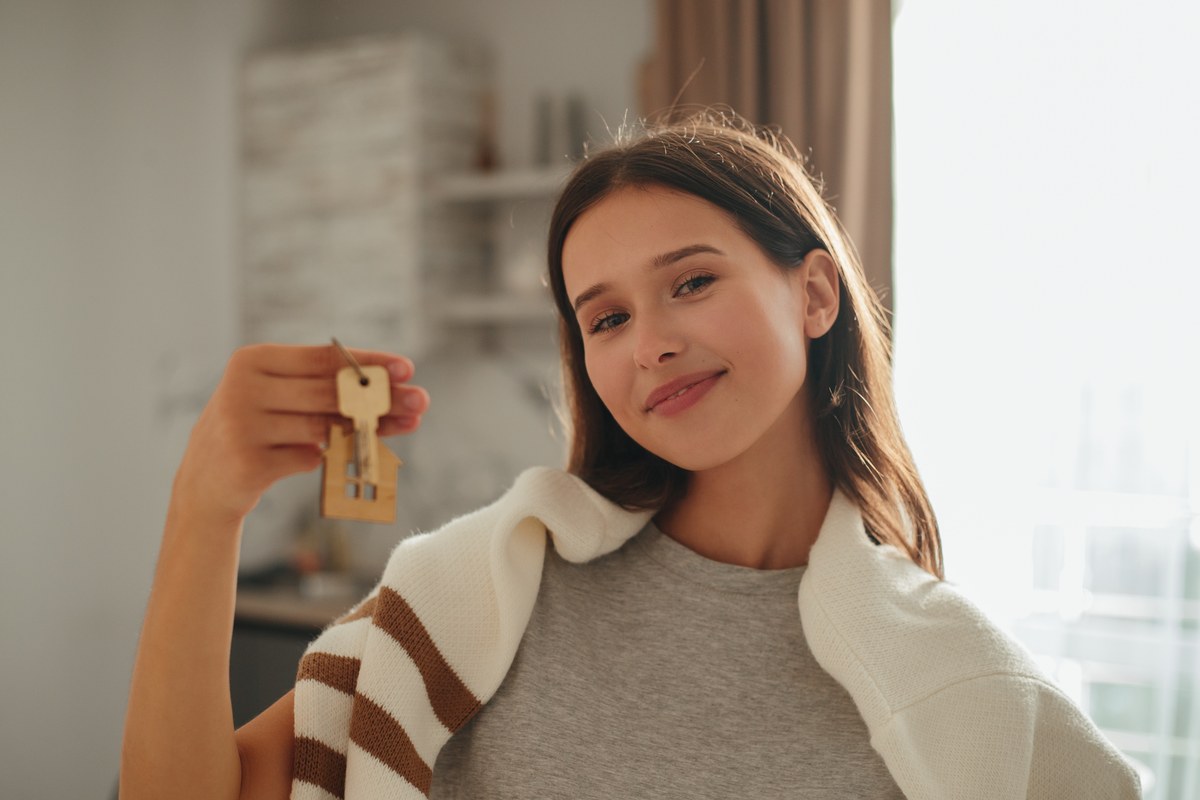 Young woman holding up a set of house keys in a bright flat